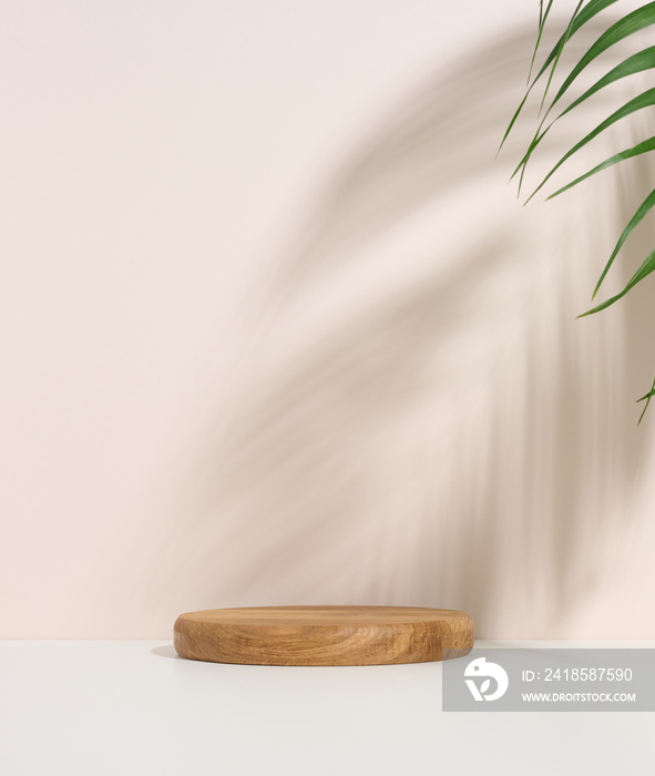 stage for displaying products, cosmetics with a round wooden podium and a green palm leaf. Shadow on
