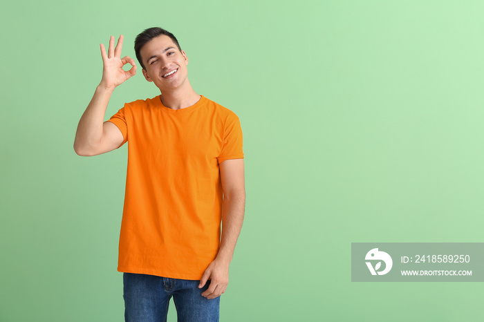 Handsome young man in orange t-shirt showing OK on color background