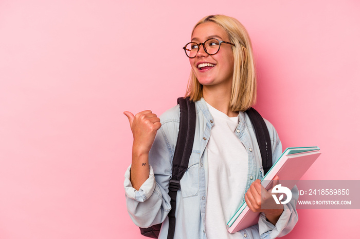 Young venezuelan student woman isolated on pink background points with thumb finger away, laughing a