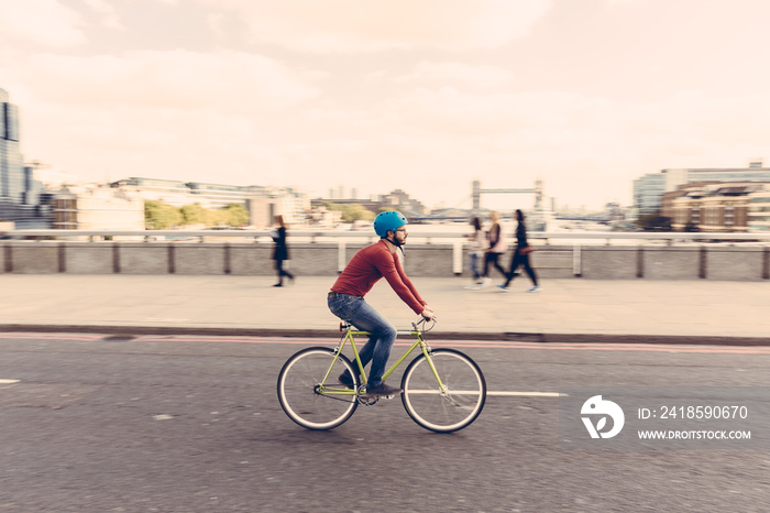 Hipster man cycling on London bridge with fixed gear bike