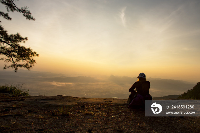 一个女人安静地坐在悬崖边，看着清晨的山谷和山脉的特写