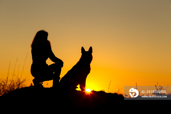 日落时，一名妇女带着一只狗在田野里散步，宠物坐在女孩腿附近，享受大自然