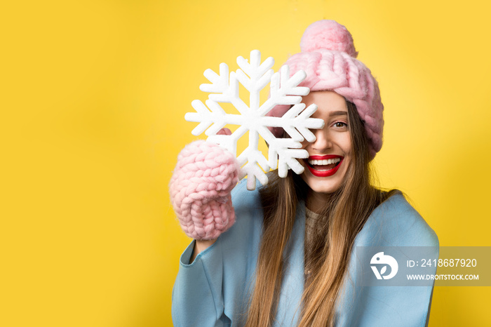 身穿彩色冬装的快乐女子手持美丽的雪花站在黄色的背景上