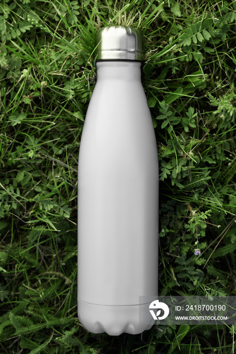 Stainless thermos water bottle isolated on green grass outdoor. White matte color. Vertical photo wi