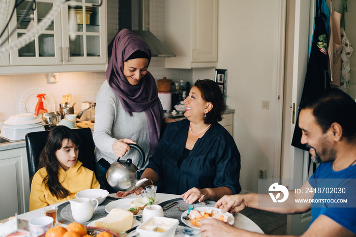 Woman serving tea to family at dining table during breakfast at home