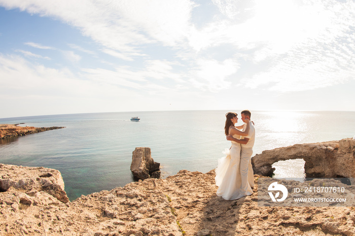 Elegant smiling young bride and groom walking on the beach, kissing and having fun, wedding ceremony