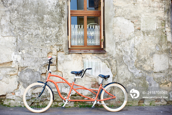 现代舒适的橙色双人自行车，白色车轮，靠在旧的灰泥裂缝上