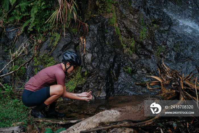 A young female cyclist is washing her hands by the creek