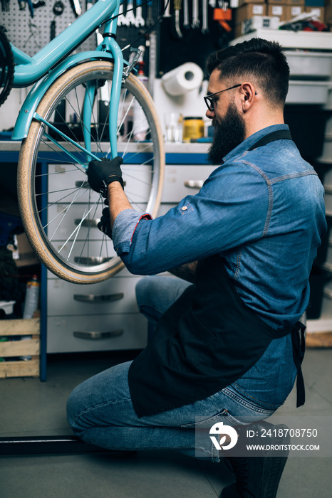 年轻的胡子自行车技工在车间修理自行车。