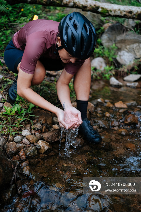 A young female cyclist is washing her hands by the creek