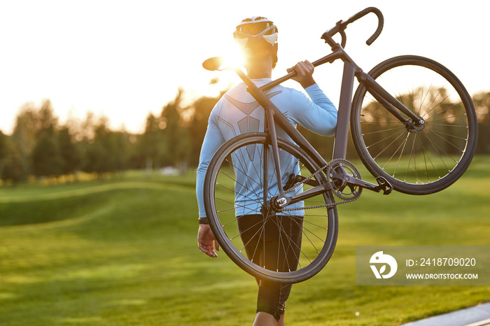 Strong athletic man in sportswear carrying his bicycle and watching amazing sunset after cycling in 