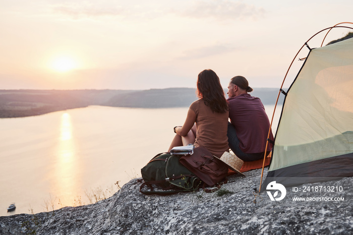 Photo of happy couple sitting in tent with a view of lake during hiking trip. Travel Lifestyle adven