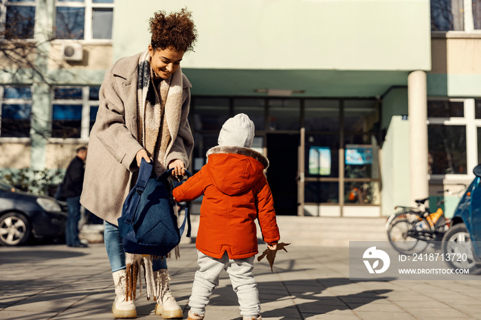 A babysitter preparing a little boy for the kindergarten while standing in the schoolyard.