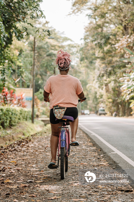 Imagen vertical desde atrás de una joven mujer afroamericana con cabello rosado andando en bicicleta