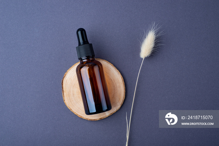 Amber glass dropper bottle with black lid on on the wooden podium with dry plants on grey background