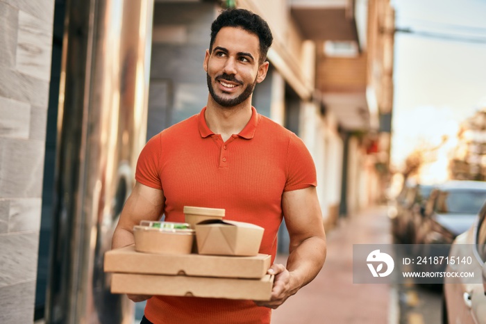 Young hispanic man smiling happy holding take away food at the city.