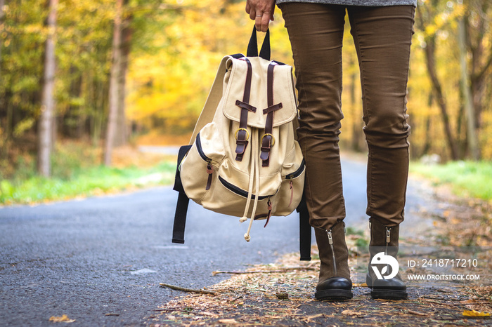 Woman with backpack wearing hiking boots is standing on road in autumn forest. Travel concept