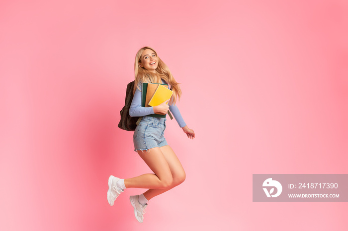 Cheering teen girl jumping over pink studio wall