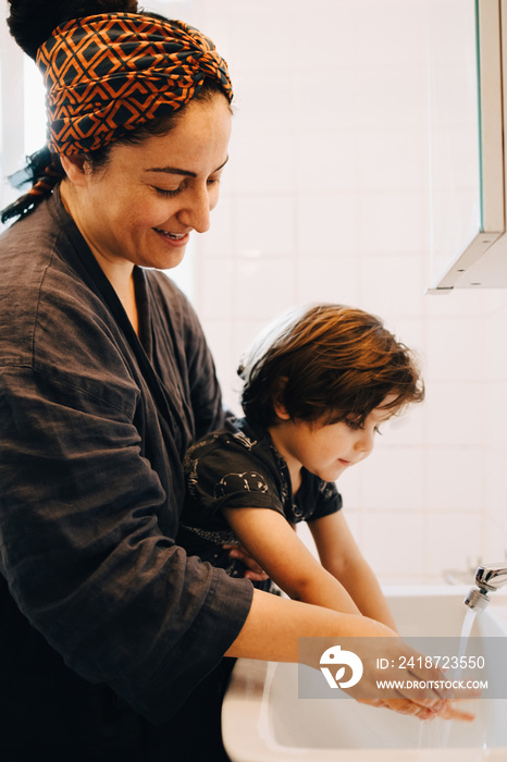 Smiling mother washing boys hands in sink at bathroom