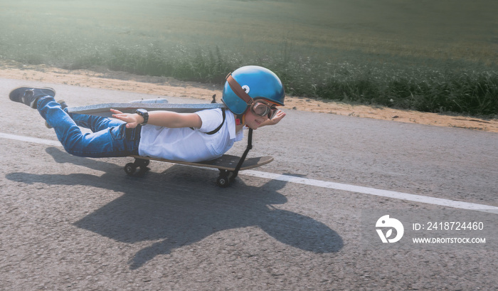 一个戴着头盔、长着泡沫塑料翅膀的小男孩在乡村道路上玩滑板，假装是一个