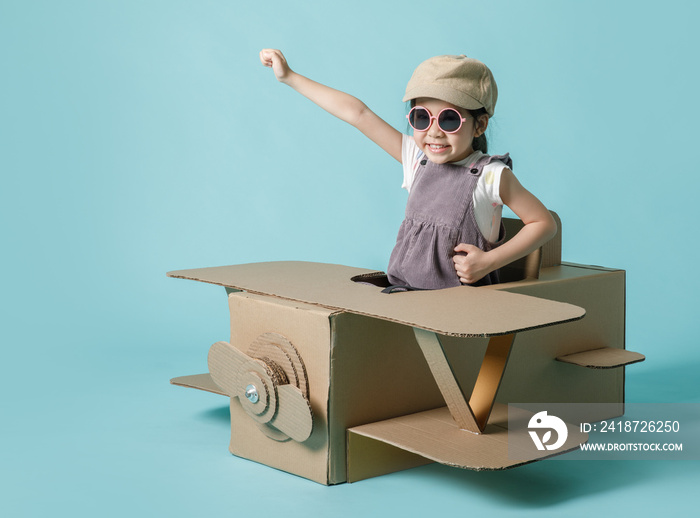 Asian little child girl playing with cardboard toy airplane handicraft isolated on blue background, 