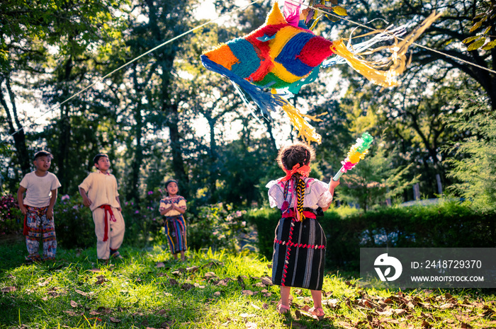 La niña va a romper la piñata por su cumpleaños en un parque.