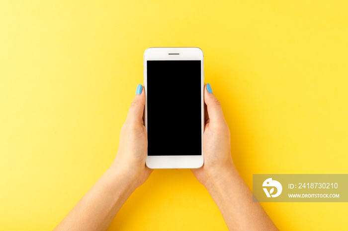 Overhead shot of woman’s hands holding mobile phone with empty screen on yellow background. Top view