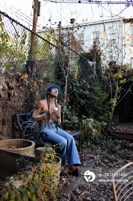 indigenous non-binary artist drinking tea in urban garden in autumn