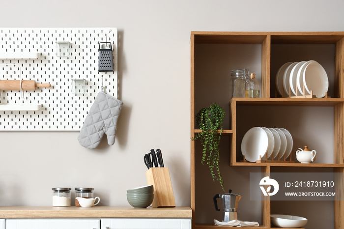 Wooden shelving unit with dishware, coffee maker and houseplant near light wall in kitchen