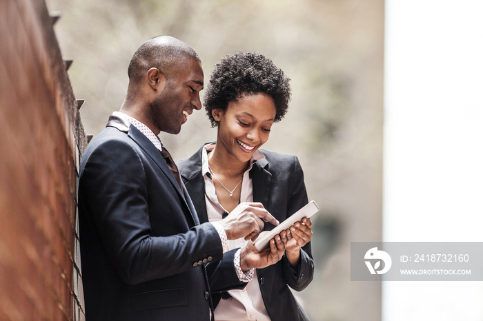 Man and woman using digital tablet together on street