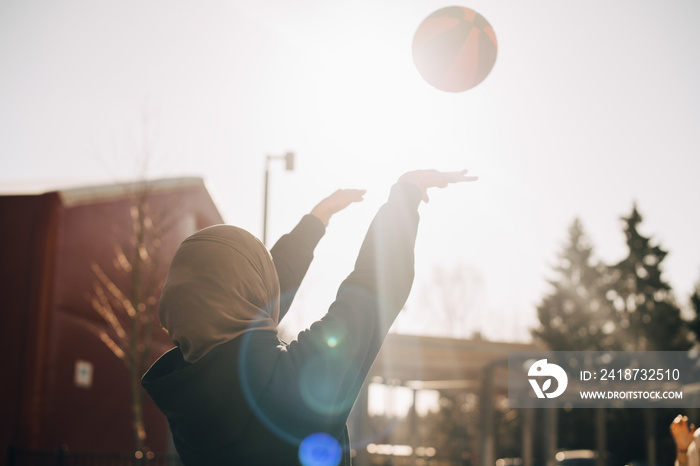 Teenage girl wearing hijab throwing ball in mid-air on sunny day