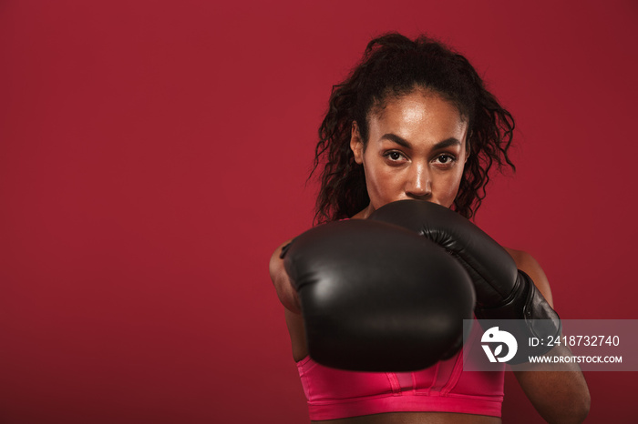 Serious strong young african sports woman boxer posing isolated over red wall background make boxing