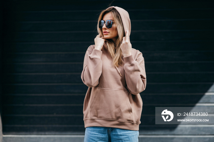 Fasion blonde woman in brown oversize hoodie, glasses and blue jeans, mockup for logo or branding de