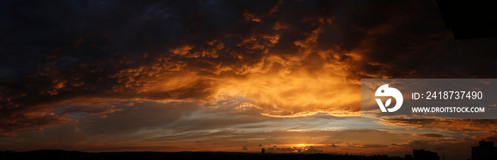 High resolution stormy sunset panorama. Epic clouds highlighted gold by setting sun.