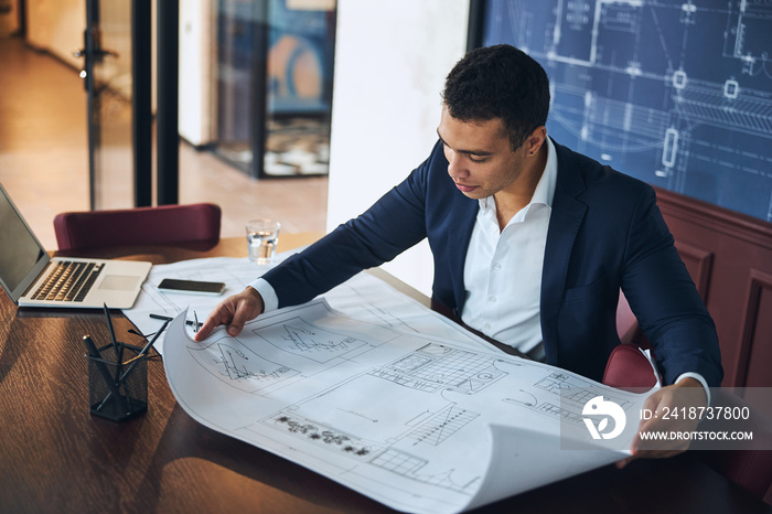 Dark-haired professional engineer scrutinizing a technical drawing