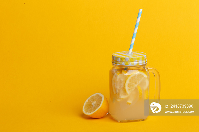 A jar of homemade lemonade and lemons on a yellow background.