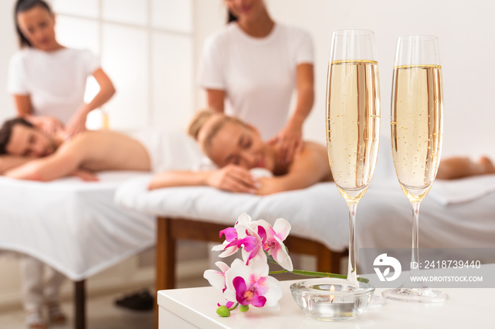 Couple Enjoying Massage, Spa Composition With Champagne Flutes And Flowers