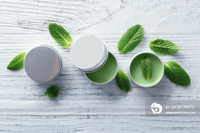 Containers with lemon balm salve and leaves on wooden table