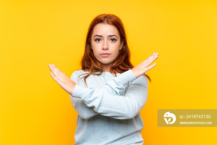 Teenager redhead girl over isolated yellow background making NO gesture