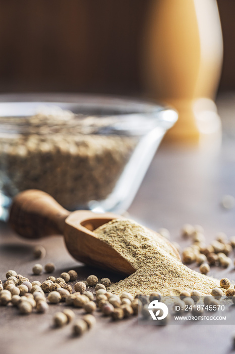 White ground pepper and whole peppercorn spice in wooden scoop.