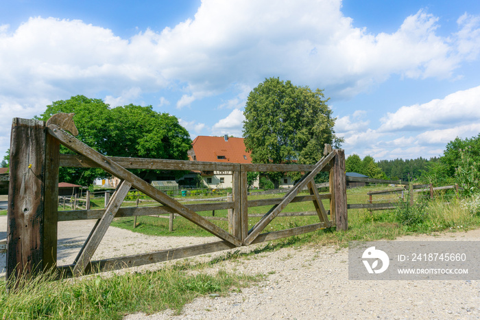 Holztor mit Pferdemuster an einem Reiterhof mit Bauernhof im Hintergrund