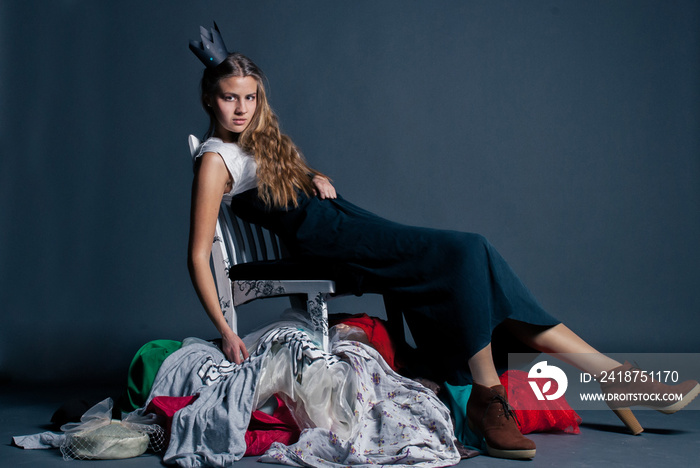girl in the crown is sitting on a pile of clothes as the queen of consumerism