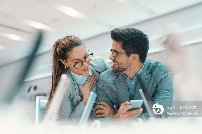 Smiling cute multicultural couple dressed formal and with eyeglasses trying out new smart phone in t