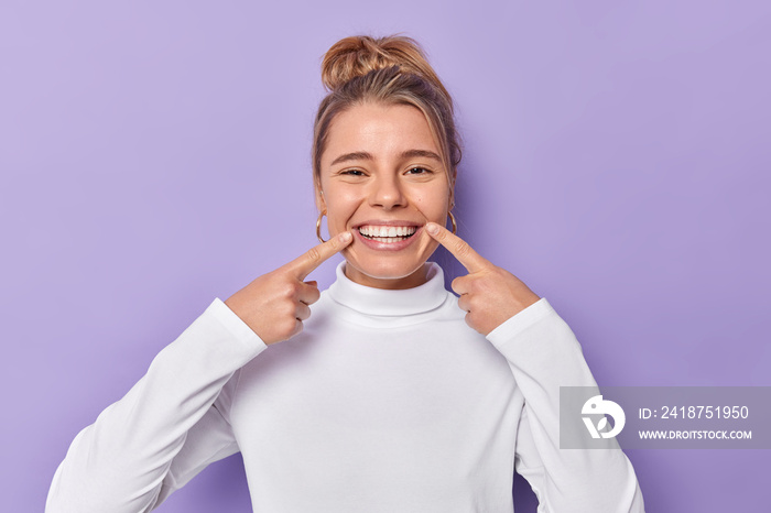 牙科护理理念。快乐的年轻金发女人用食指指着牙齿，露出灿烂的笑容。
