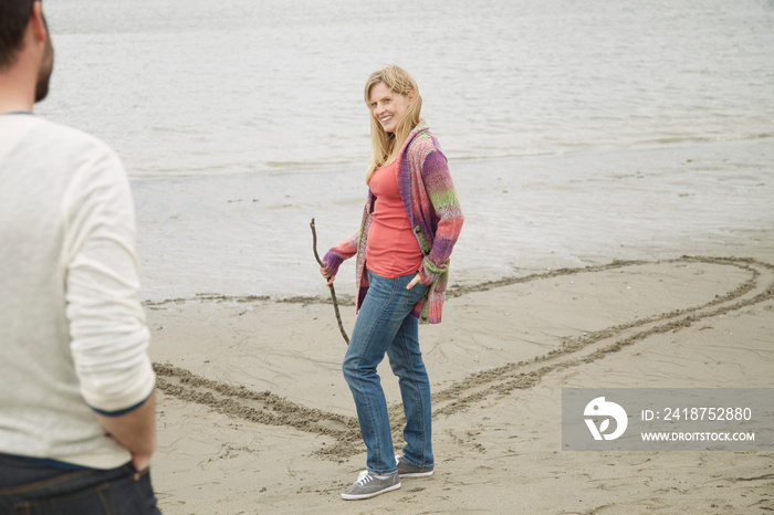 mid-adult woman drawing heart in the sand