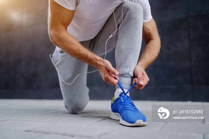 Close up of caucasian sportsman in tracksuit tying shoelace while kneeling outdoors.