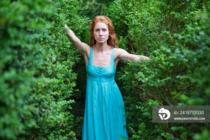 Red haired woman standing between hedges