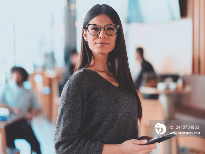 Portrait of pretty young businesswoman looking at camera while holding digital tablet standing in th