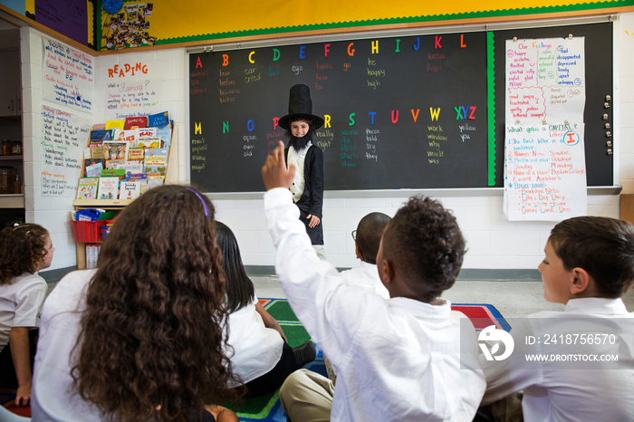 Rear view of group of schoolchildren (8-9, 10-11) sitting in classroom watching costumed presentatio