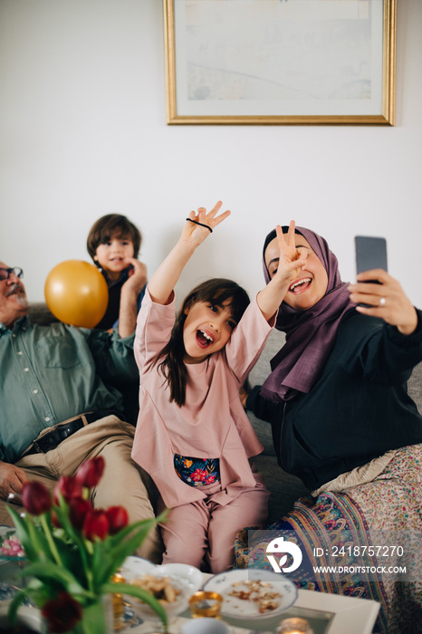 Cheerful girl posing with family while mother taking selfie on smart phone during party